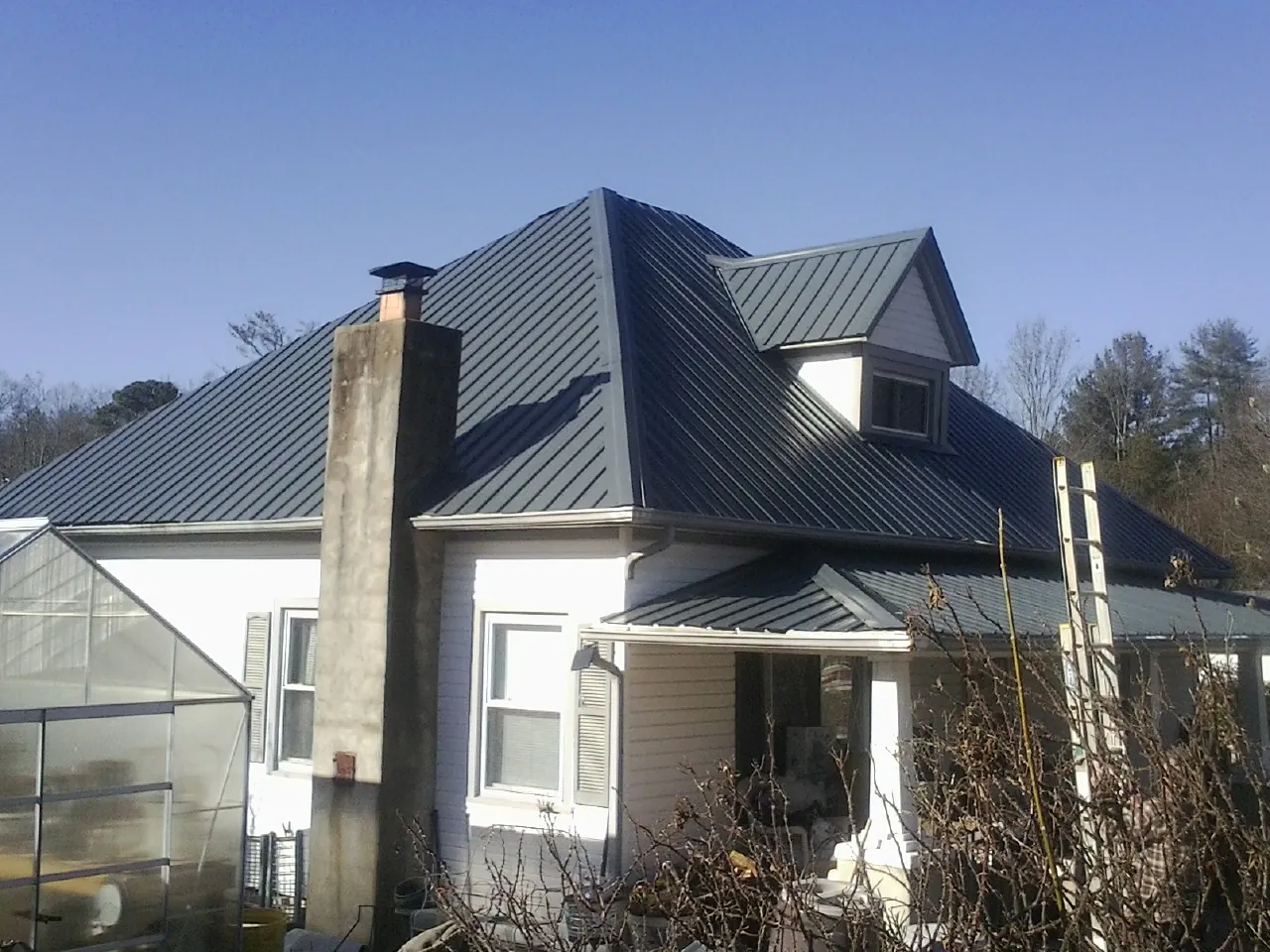 Dark blue standing seam metal roof on a white farmhouse with dormer — Slate & Tile Roof Repair by Roofing Brothers in Ehrhardt