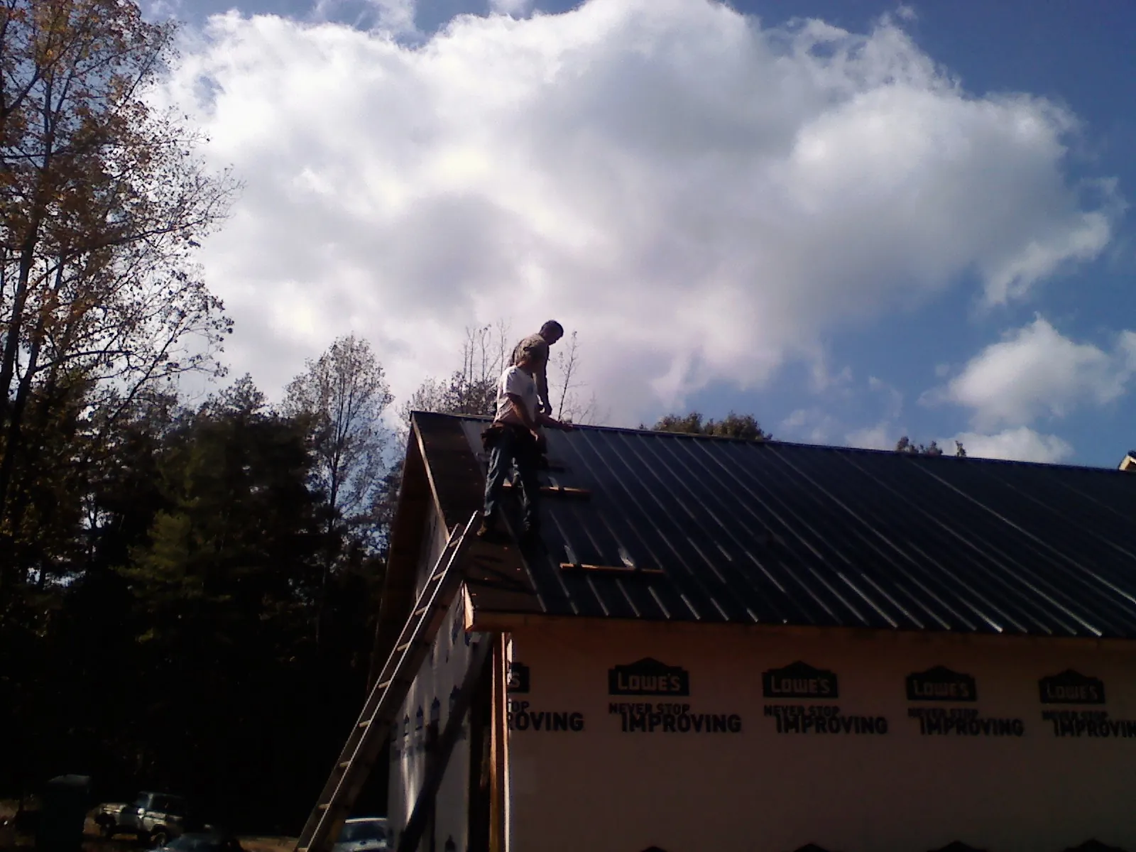 Roofer fastening dark metal panels high against a cloudy sky, from a Roof Inspection job in Ehrhardt